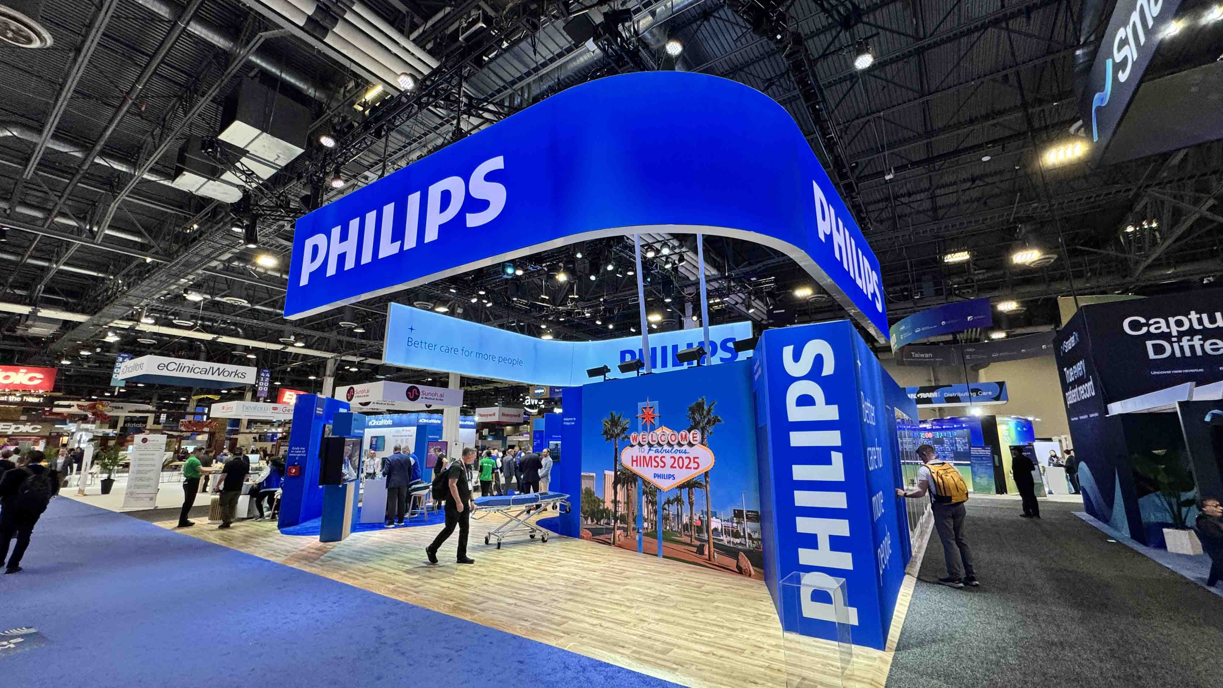 An image of a tradeshow booth. The booth is blue in color and has several large screens. The booth is Owned by Philips