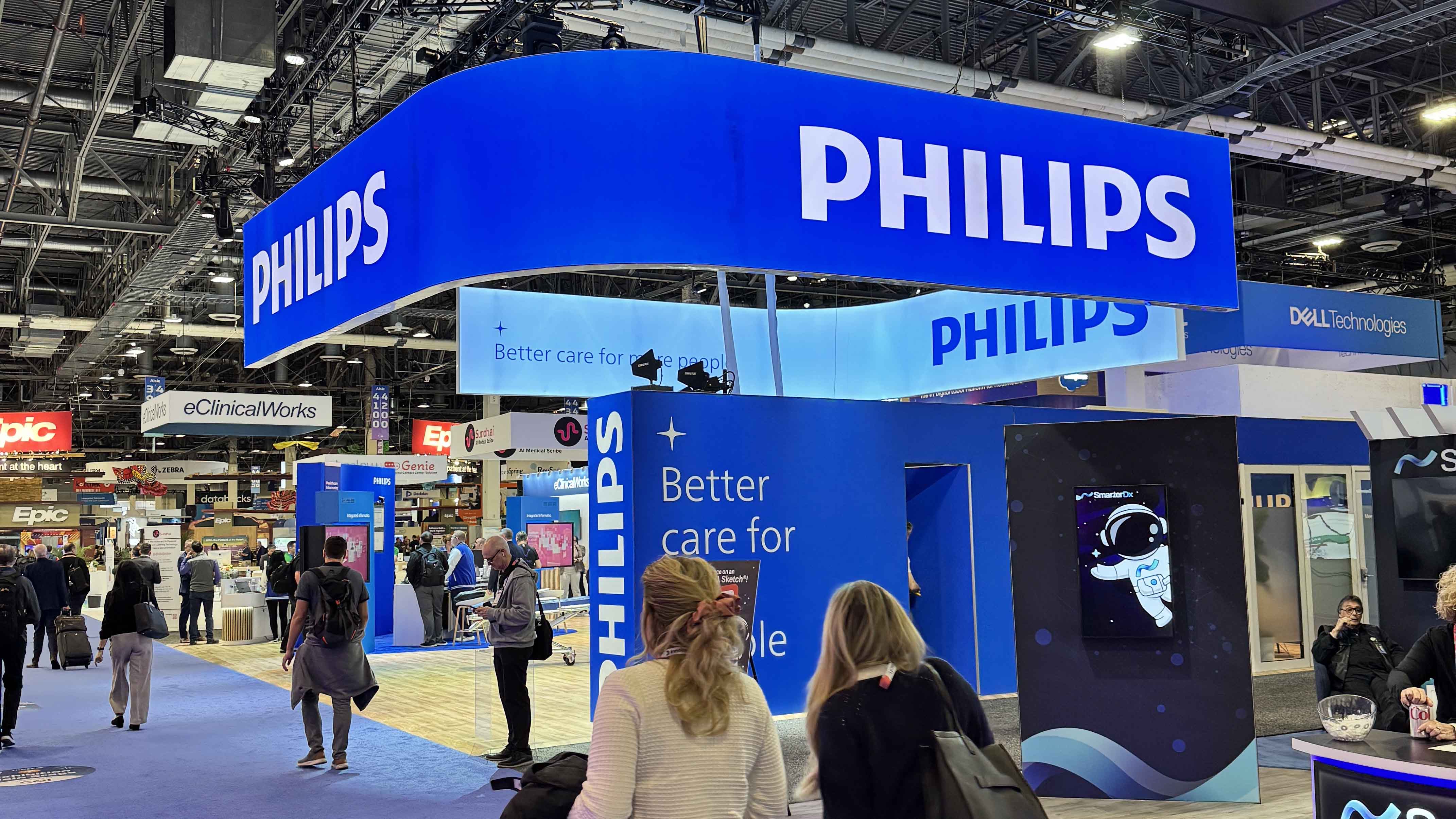 An image of a tradeshow booth. The booth is blue in color and has several large screens. The booth is Owned by Philips