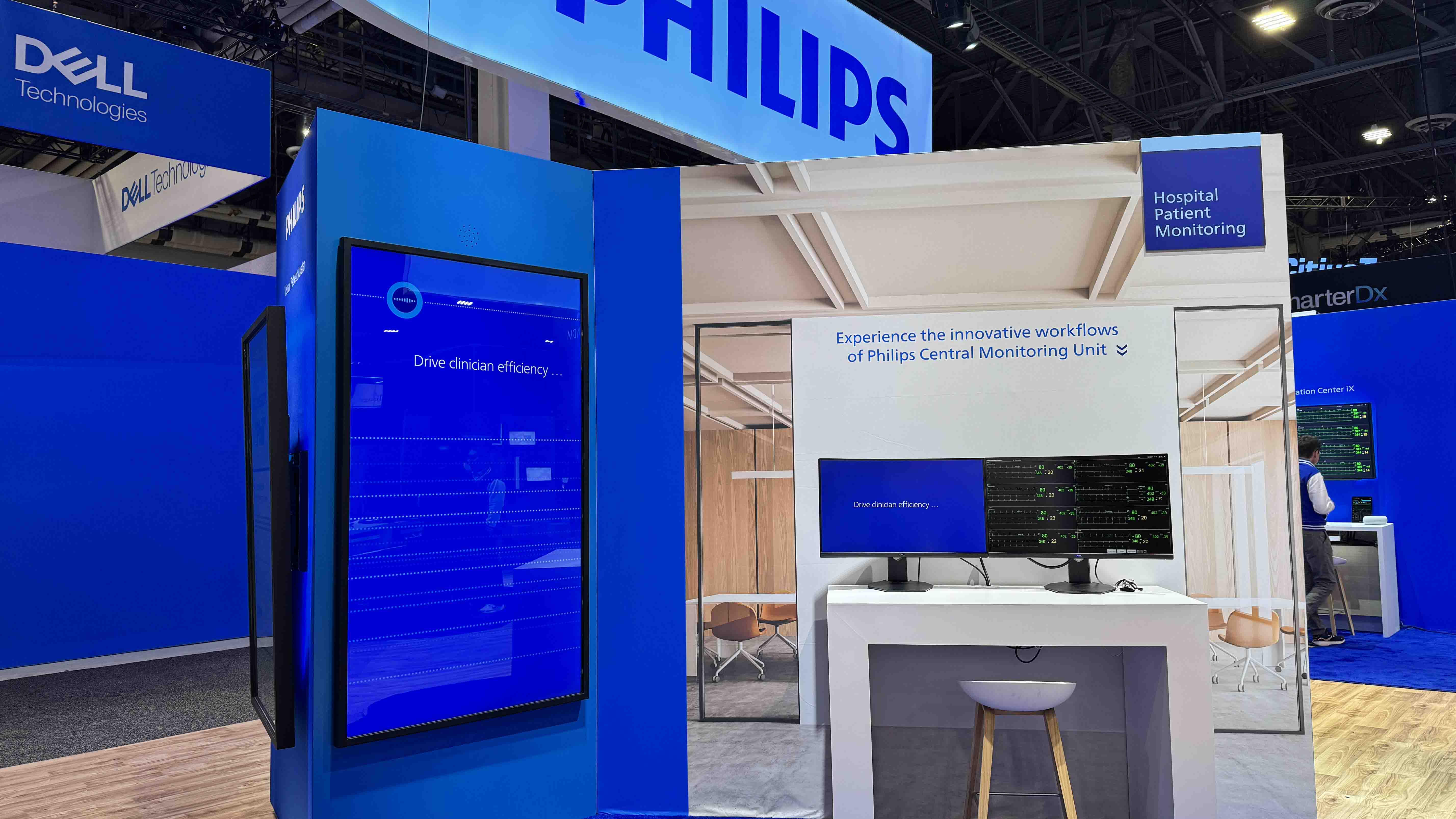 An image of a tradeshow booth. The booth is blue in color and has several large screens. scene of office space. The booth is Owned by Philips