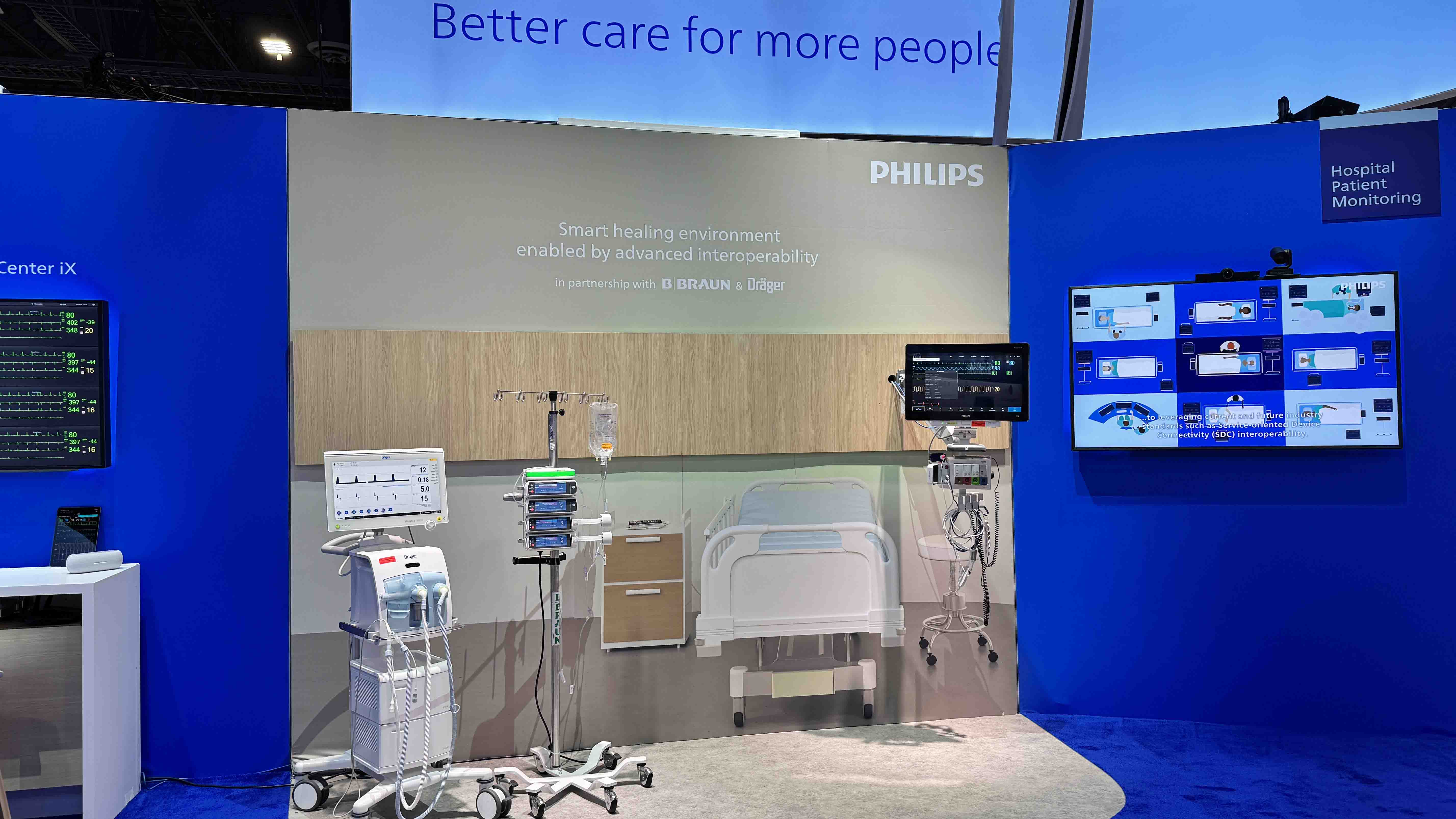 An image of a tradeshow booth. The booth is blue in color and has several large screens. Scene of hospital room. The booth is Owned by Philips