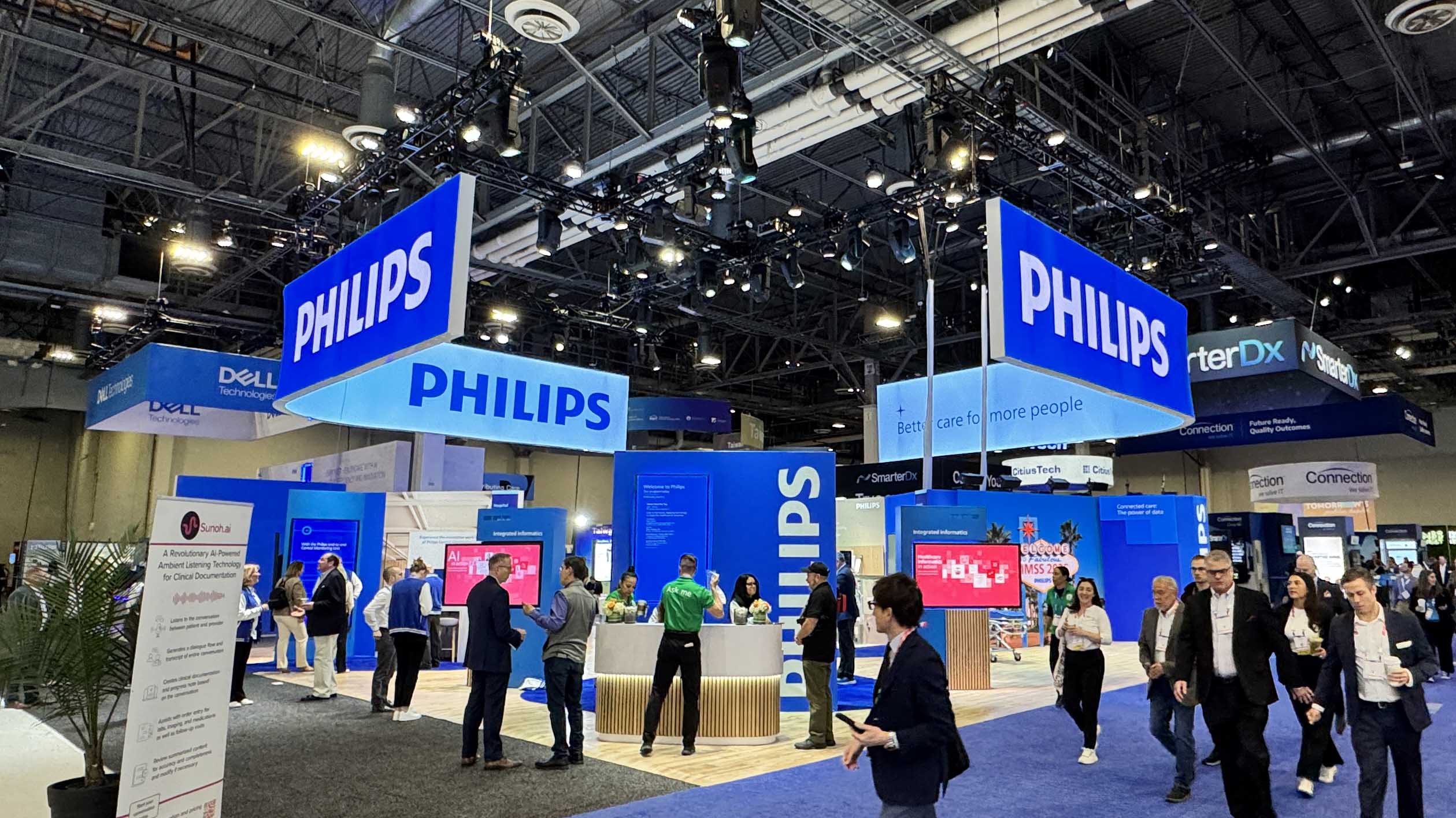 An image of a tradeshow booth. The booth is blue in color and has several large screens. The booth is Owned by Philips