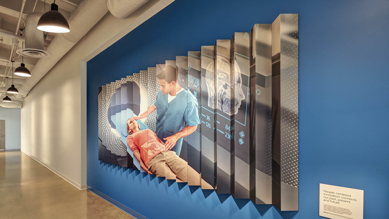 A Photograph of a lenticular image on a wall in a hall way. The lenticulare has an image of a futuristic CT or MR machine in color.