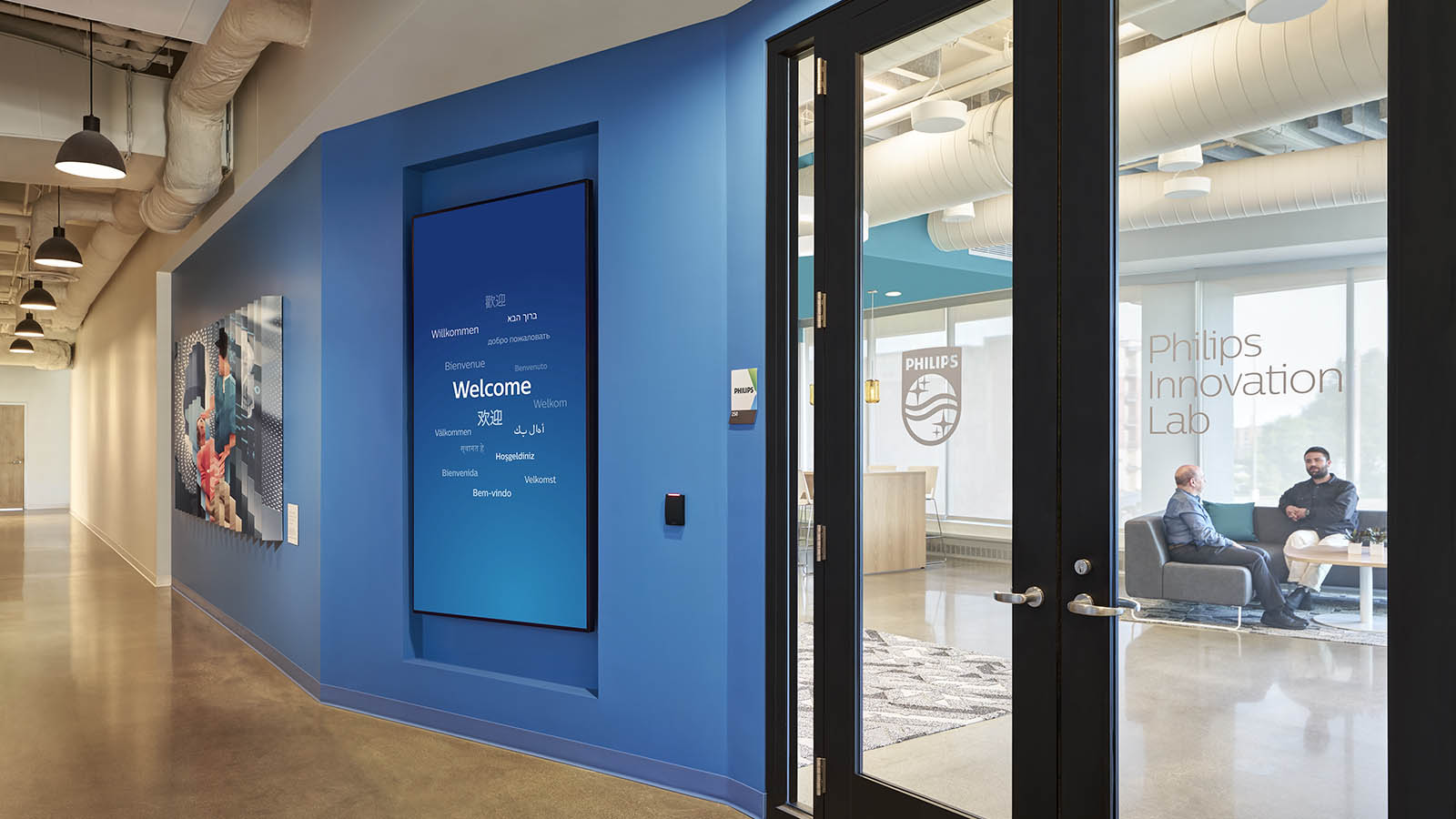 A photograph of a door to an office space within a building. There is a large blue screen and glass doors woth typography and a logo on the doors.